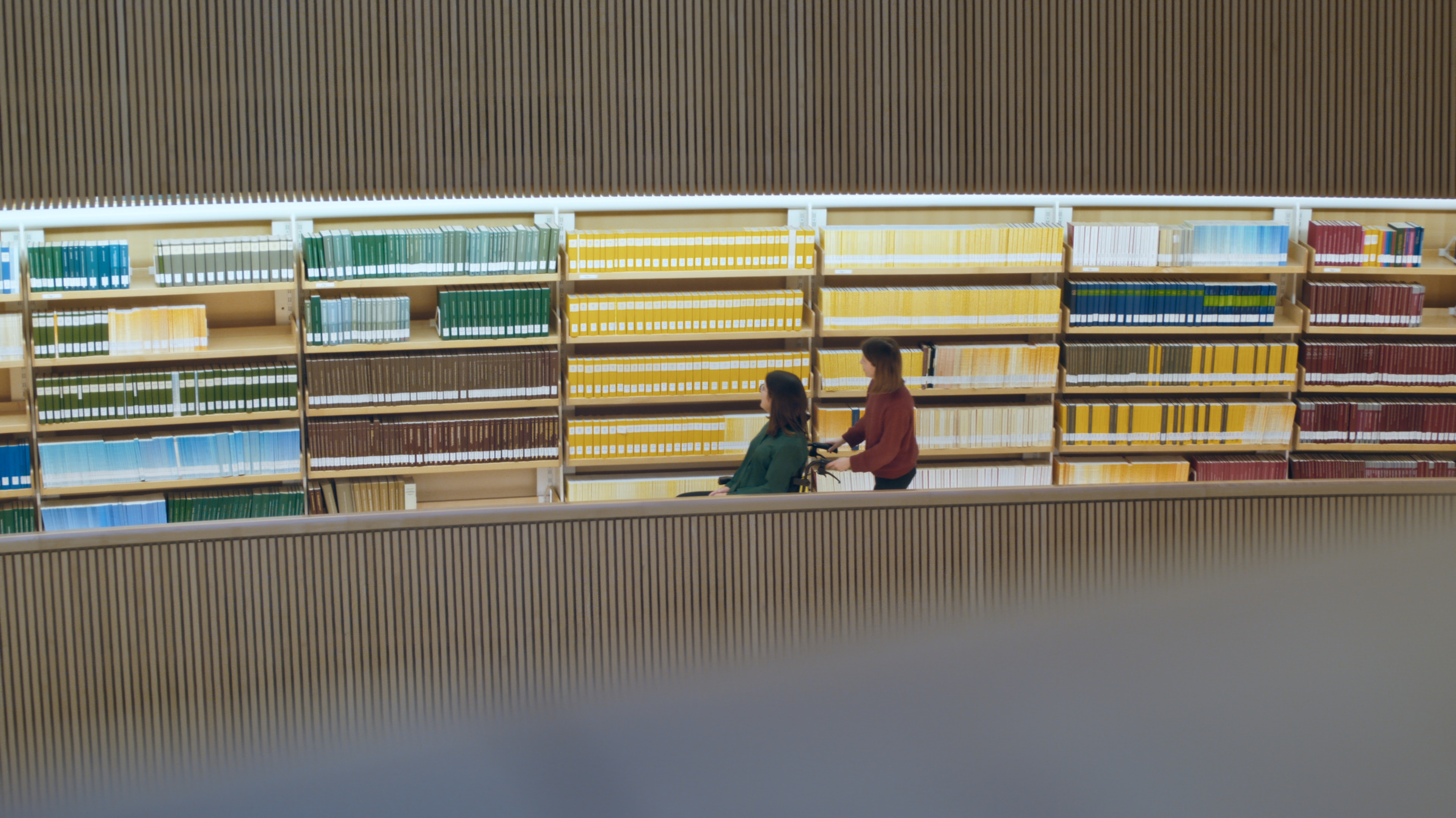 A woman is showing the university library to a woman using a wheelchair